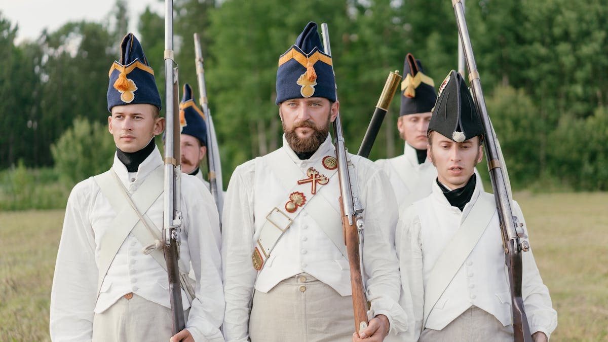 Soldiers marching in historical military uniforms reenact past events outdoors.